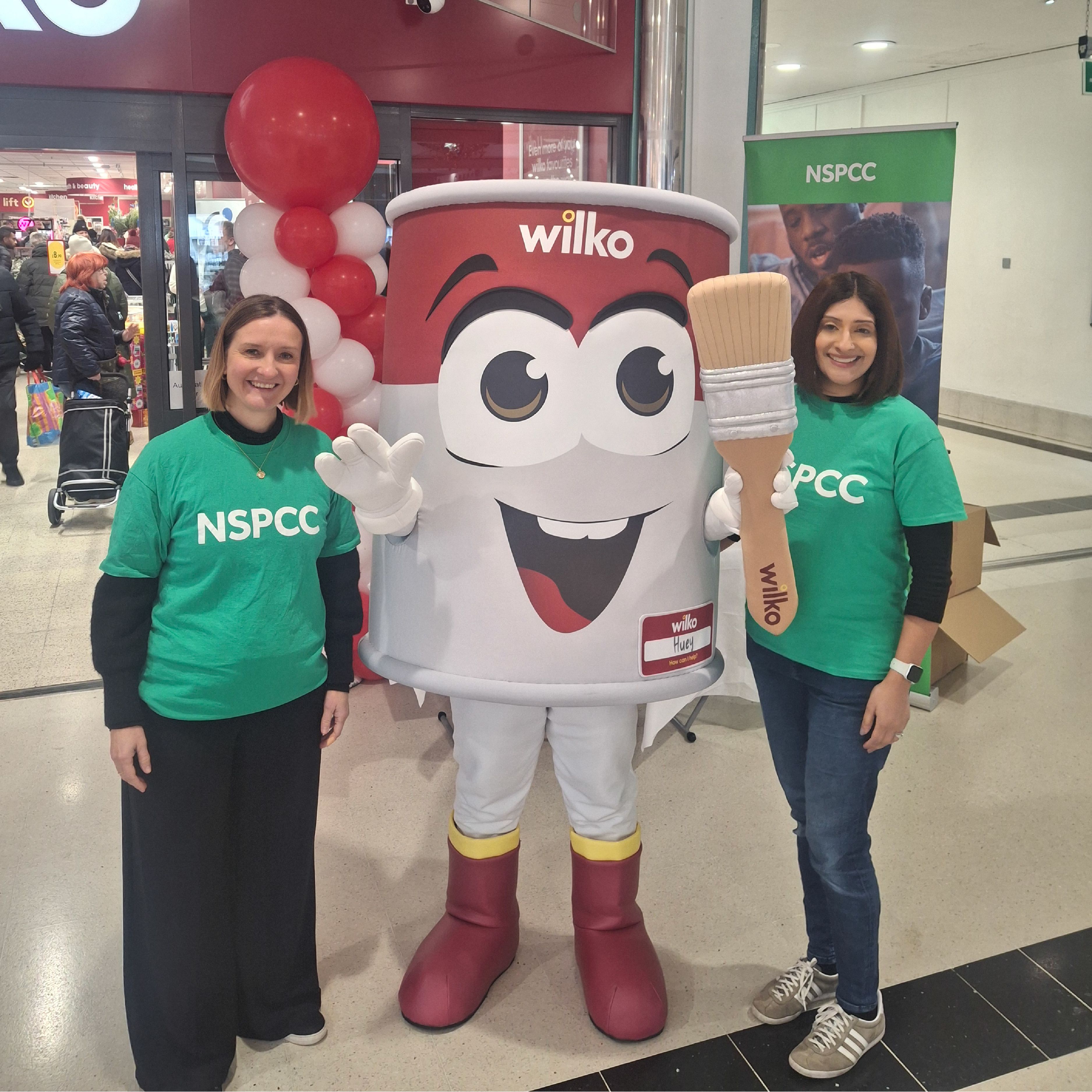 Two NSPCC staff stood outside a Wilko store with a Wilko paint pot mascot