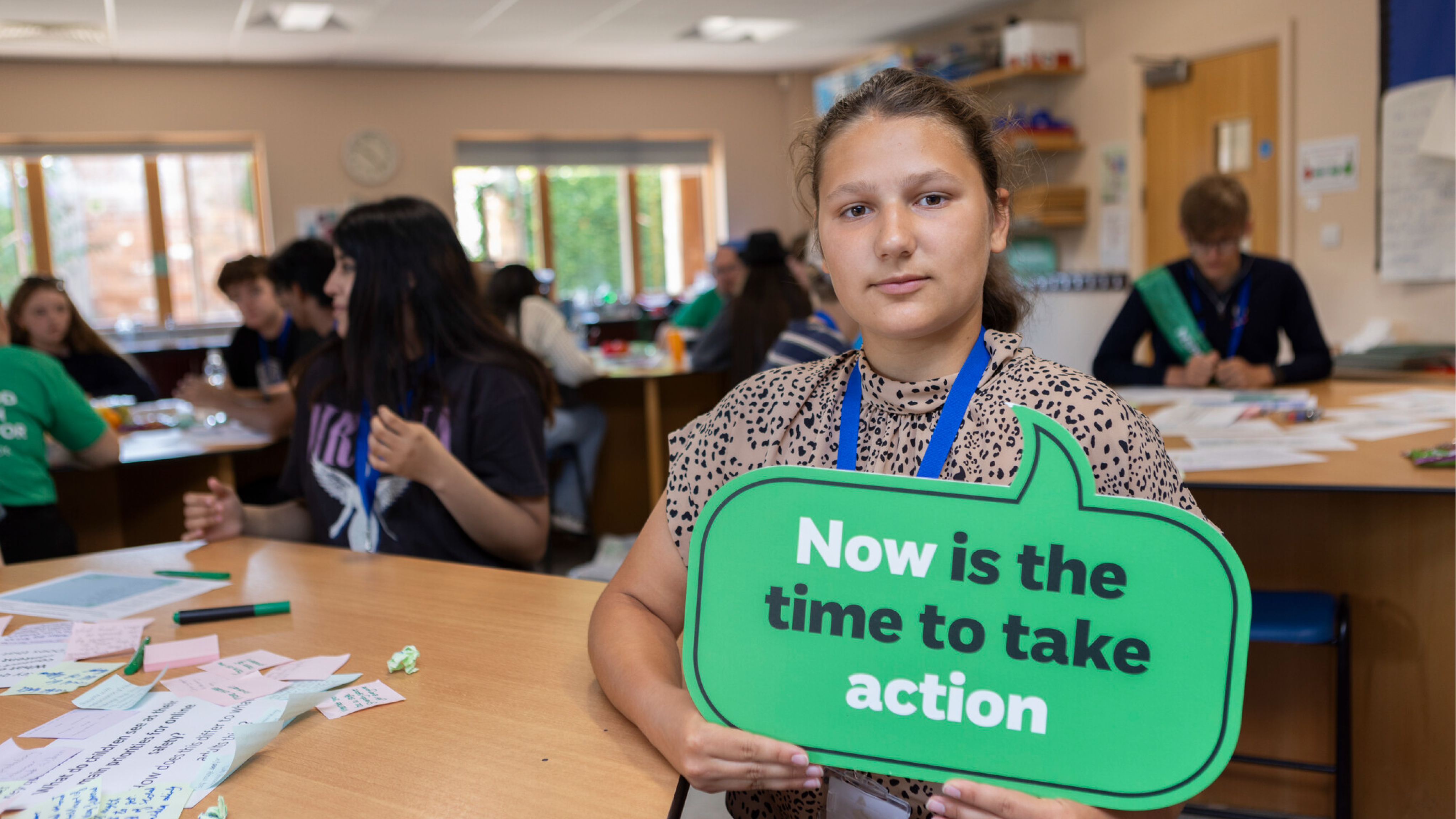 A teenage girl holding a sign that says 'Now is the time to take action'