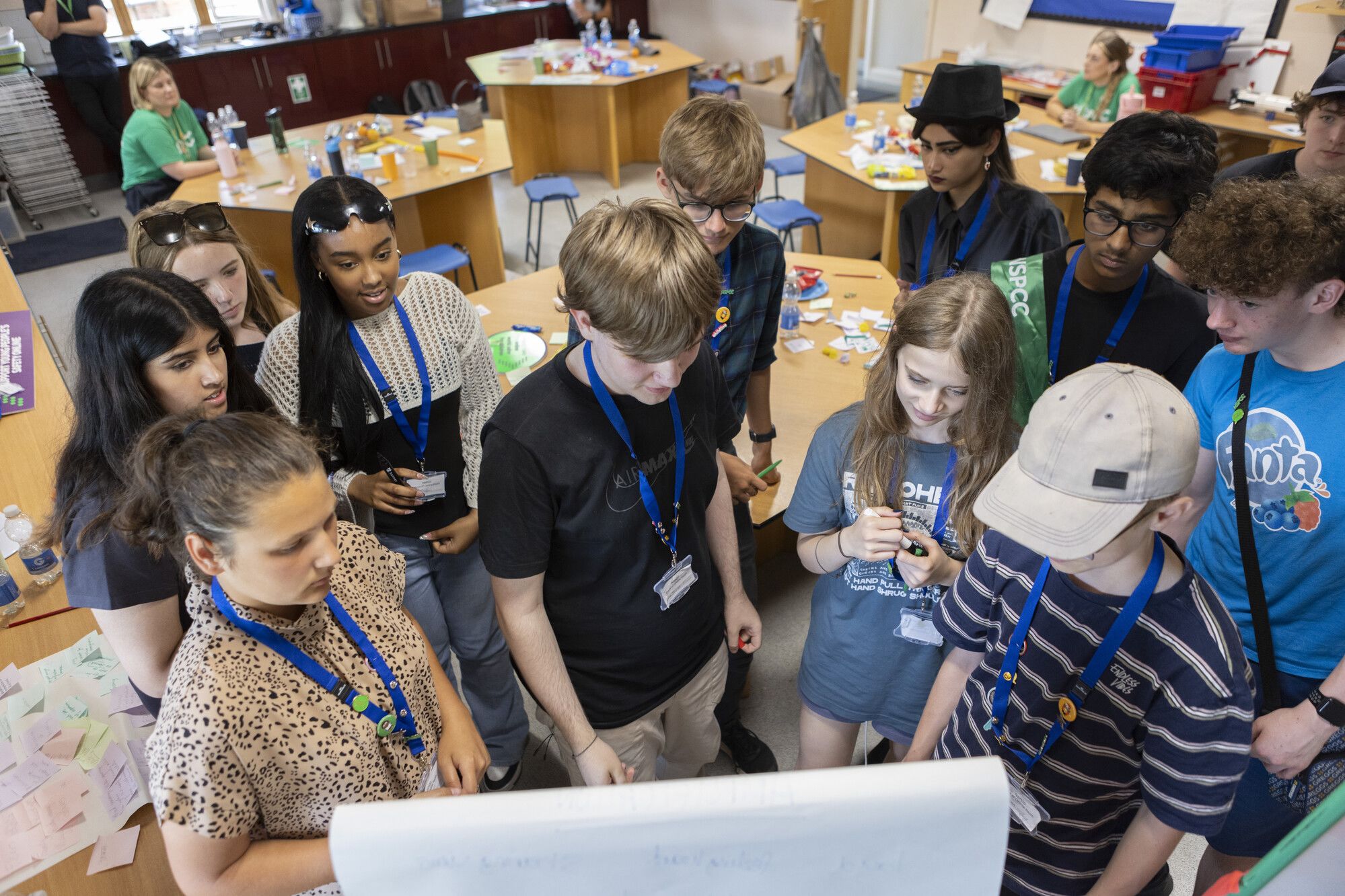 A group of young people wearing lanyards, gathered around a flipchart