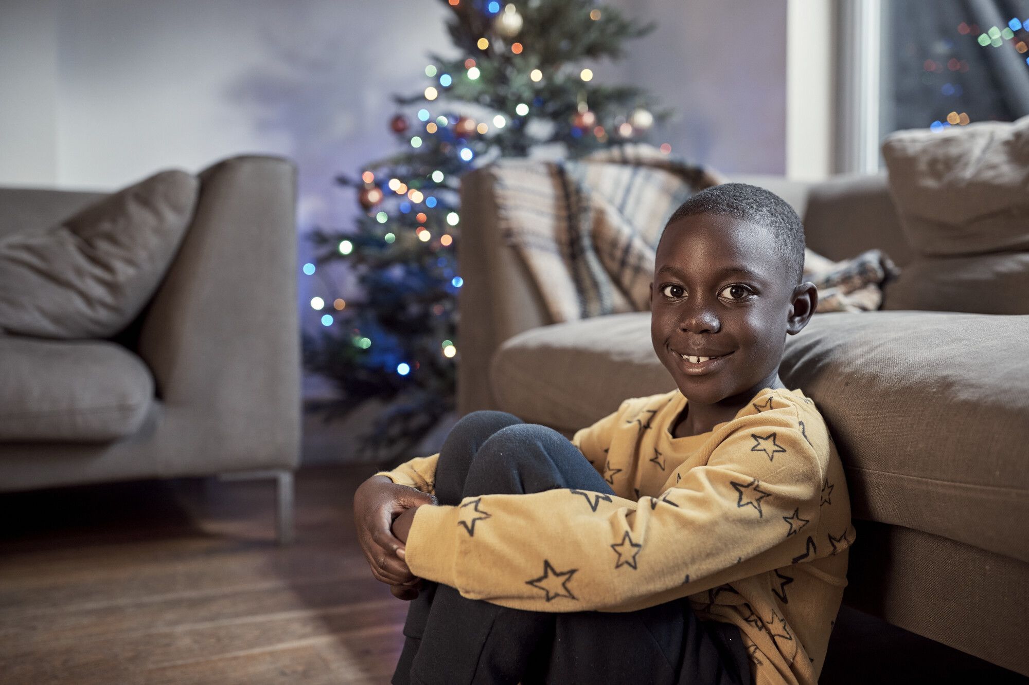 A boy sat in front of a Christmas tree, smiling